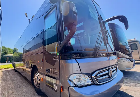 Gray tour bus parked in a lot, front-left view showing the Mercedes emblem and bus number 5023, with another bus visible in the background.