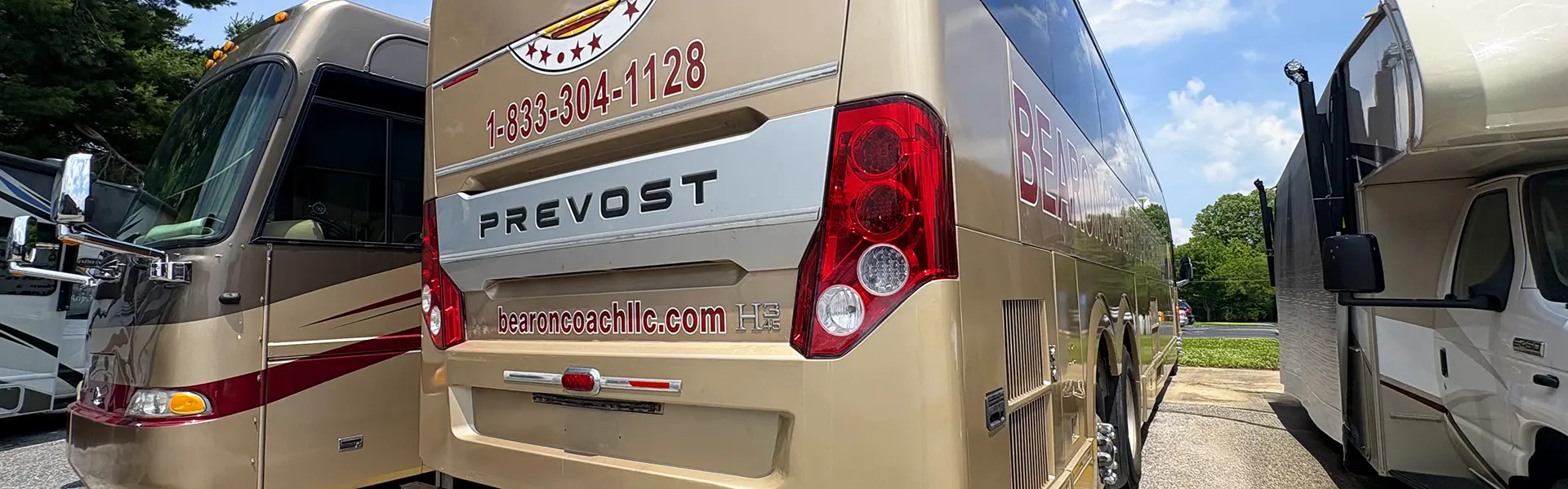 Rear view of a beige Prevost tour bus with red taillights, bearing the website bearoncoachllc.com and a phone number 1-833-304-1128 on the back.