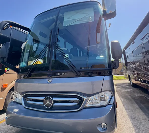 Front view of a gray Mercedes-Benz coach bus parked between other buses on a sunny day.